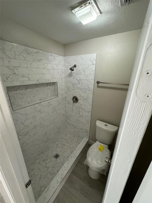 bathroom featuring a tile shower, toilet, and a textured ceiling