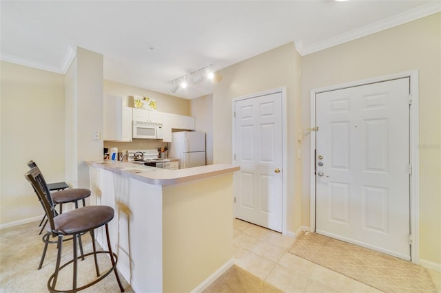 kitchen featuring kitchen peninsula, light tile patterned flooring, white appliances, a breakfast bar area, and white cabinets