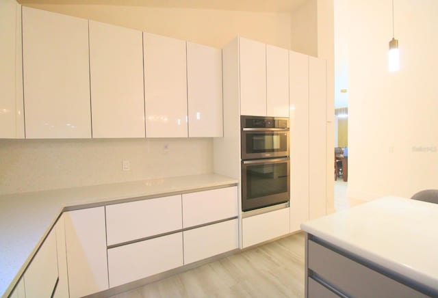 kitchen featuring decorative light fixtures, light wood-type flooring, white cabinetry, stainless steel double oven, and lofted ceiling