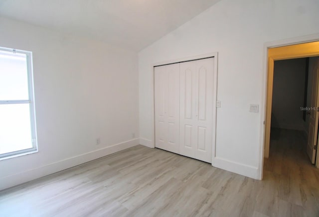 unfurnished bedroom with light hardwood / wood-style floors, a closet, and lofted ceiling