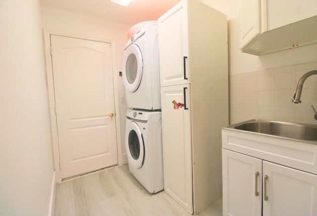 laundry room featuring cabinets, stacked washer / drying machine, sink, and light wood-type flooring