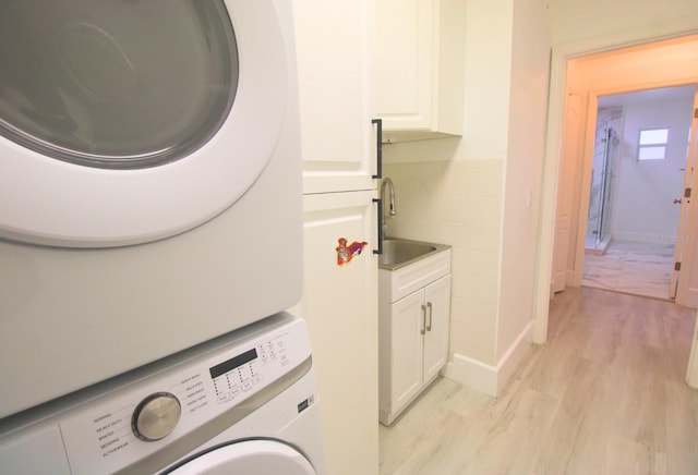 laundry room with light wood-type flooring, stacked washer / drying machine, cabinets, and sink