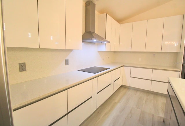 kitchen featuring black electric stovetop, white cabinets, backsplash, wall chimney exhaust hood, and lofted ceiling