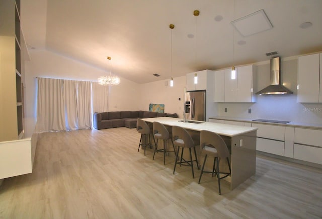 kitchen featuring wall chimney range hood, white cabinets, stainless steel fridge with ice dispenser, and a center island with sink