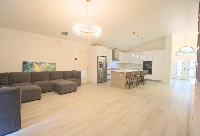 living area with high vaulted ceiling, visible vents, light wood-style floors, french doors, and an inviting chandelier