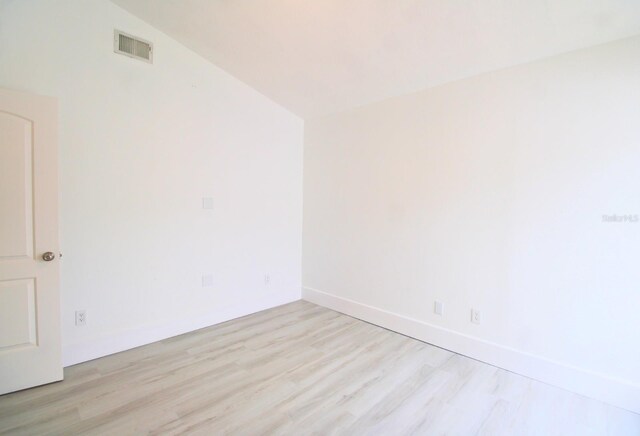 spare room with visible vents, vaulted ceiling, light wood-style flooring, and baseboards