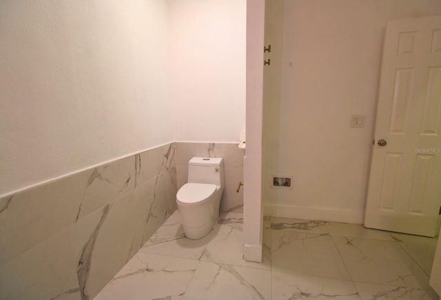 bathroom with marble finish floor, wainscoting, and toilet