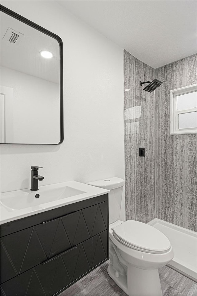 bathroom with toilet, a tile shower, hardwood / wood-style flooring, and vanity