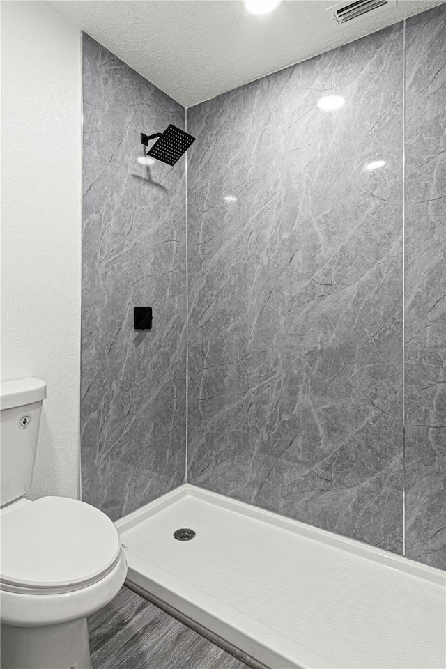 bathroom with toilet, wood-type flooring, a textured ceiling, and a tile shower