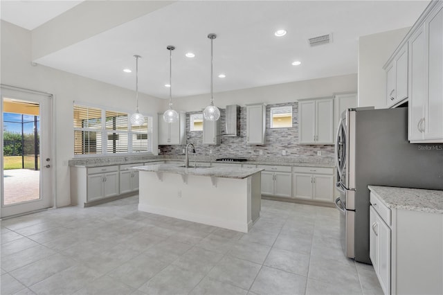 kitchen featuring light stone counters, sink, wall chimney range hood, and a center island with sink