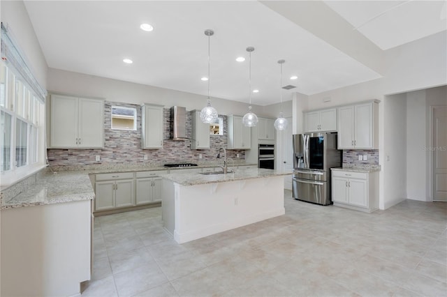 kitchen with white cabinetry, wall chimney range hood, sink, stainless steel appliances, and a center island with sink