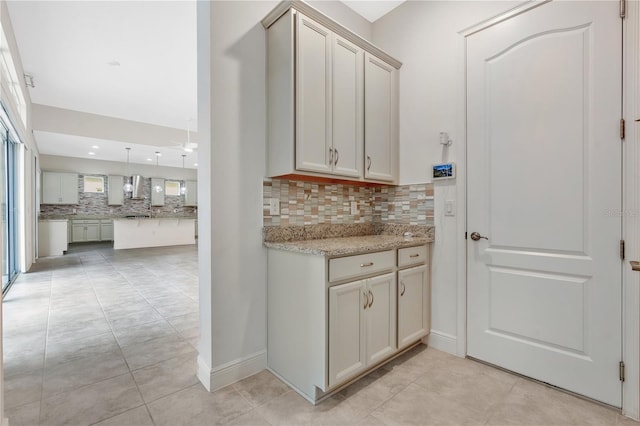 kitchen featuring tasteful backsplash, wall chimney range hood, pendant lighting, and light stone counters