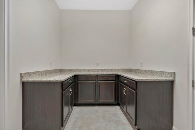 kitchen featuring dark brown cabinetry, light stone counters, and light tile patterned flooring