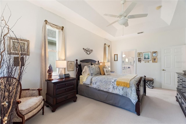 bedroom featuring ceiling fan, connected bathroom, a tray ceiling, and light colored carpet