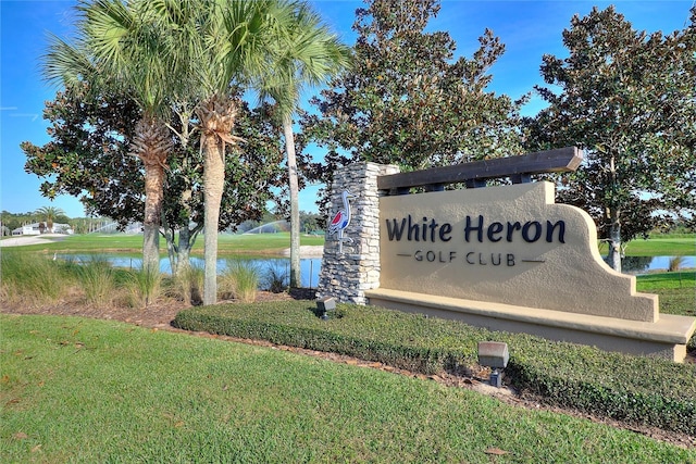 community / neighborhood sign featuring a water view and a lawn