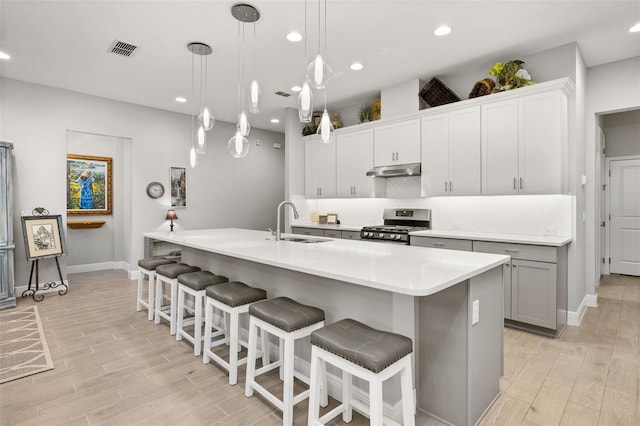 kitchen with a kitchen island with sink, sink, stainless steel stove, and decorative light fixtures