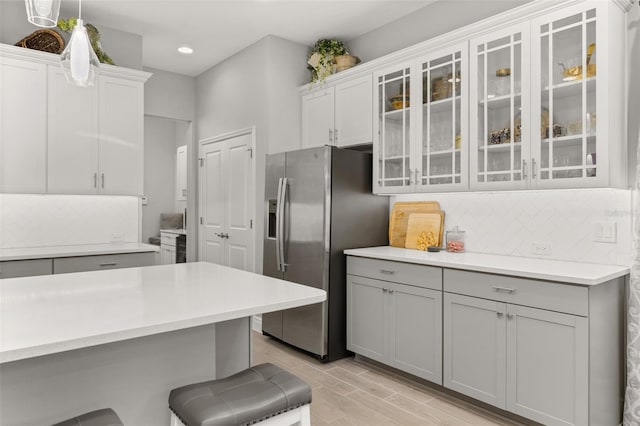 kitchen with gray cabinets, pendant lighting, tasteful backsplash, a kitchen bar, and stainless steel fridge with ice dispenser