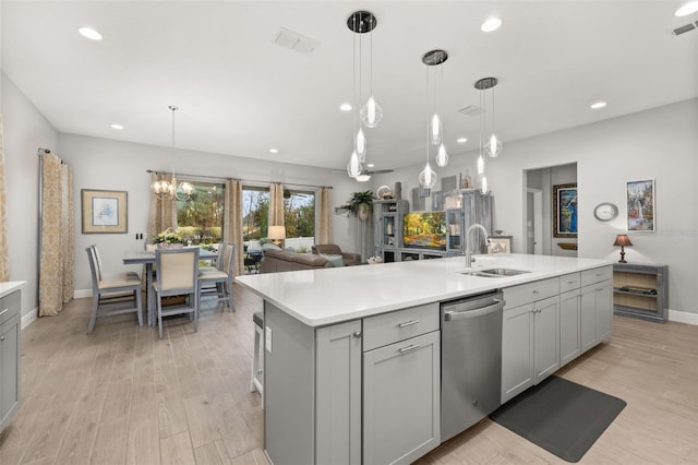 kitchen featuring an island with sink, sink, gray cabinetry, hanging light fixtures, and stainless steel dishwasher