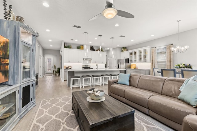 living room featuring ceiling fan with notable chandelier, sink, and light hardwood / wood-style floors