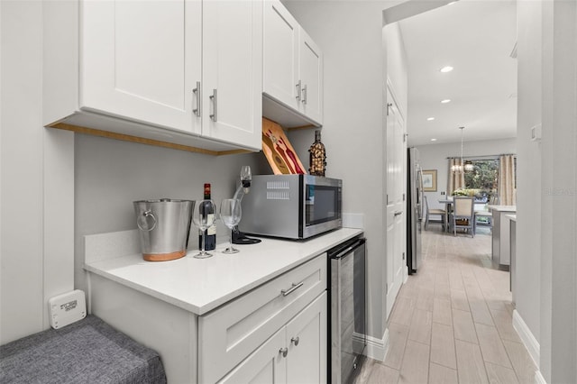 kitchen with wine cooler, decorative light fixtures, light hardwood / wood-style flooring, appliances with stainless steel finishes, and white cabinets