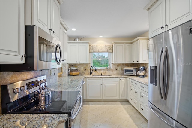 kitchen featuring appliances with stainless steel finishes, white cabinetry, sink, decorative backsplash, and light stone countertops