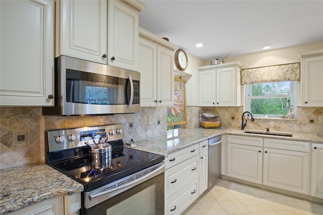 kitchen with light tile patterned flooring, sink, light stone counters, appliances with stainless steel finishes, and backsplash