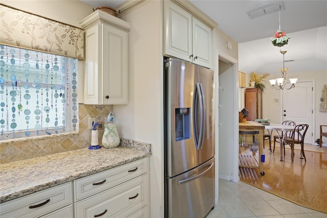 kitchen featuring stainless steel fridge, backsplash, light stone counters, light tile patterned flooring, and decorative light fixtures