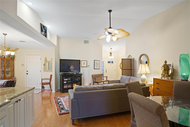 living room featuring vaulted ceiling, ceiling fan with notable chandelier, and light hardwood / wood-style floors