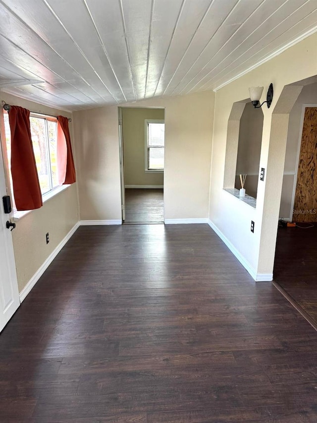 empty room featuring a healthy amount of sunlight, dark wood-style floors, and baseboards