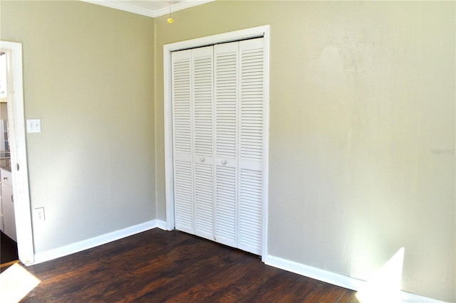 unfurnished bedroom featuring ornamental molding, a closet, dark wood finished floors, and baseboards