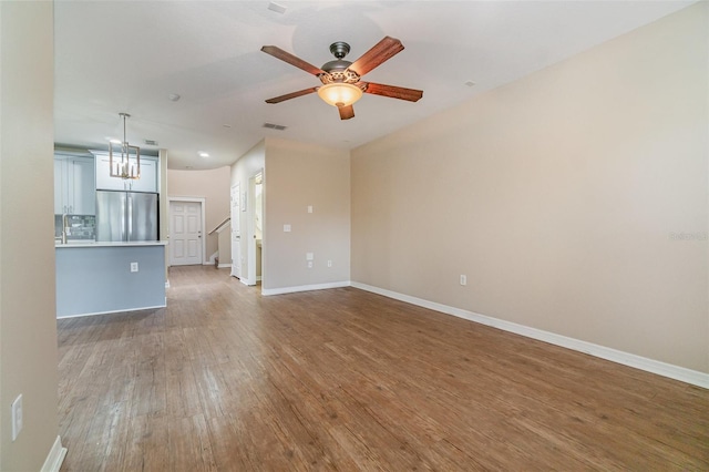 unfurnished living room featuring ceiling fan with notable chandelier and hardwood / wood-style floors