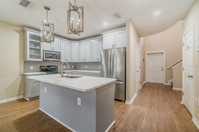 kitchen with sink, decorative light fixtures, a center island with sink, stainless steel appliances, and decorative backsplash