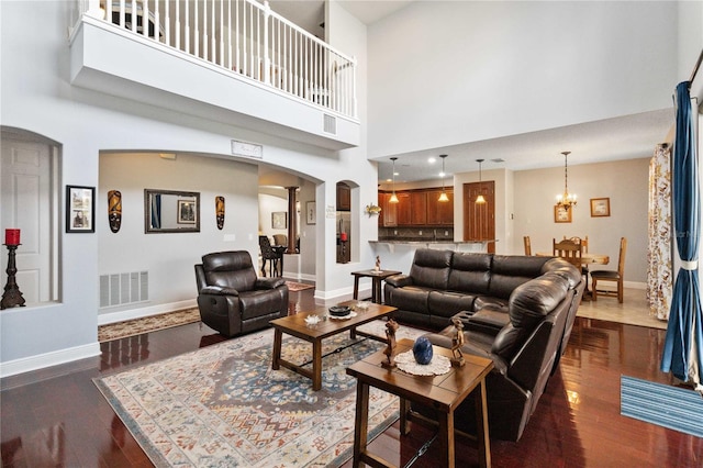 living room with dark hardwood / wood-style flooring, a notable chandelier, a towering ceiling, and ornate columns