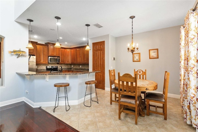 kitchen featuring a breakfast bar, hanging light fixtures, dark stone countertops, appliances with stainless steel finishes, and kitchen peninsula