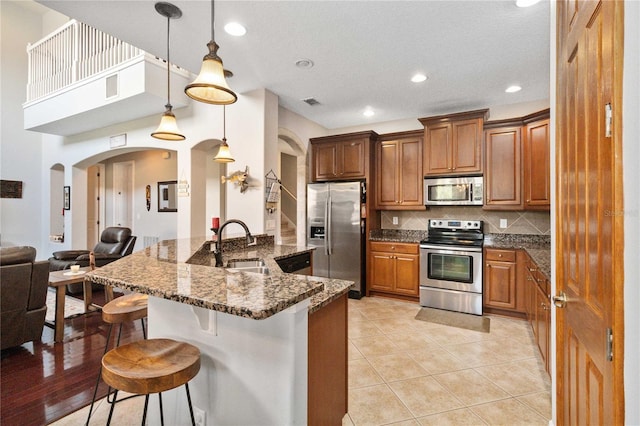 kitchen with appliances with stainless steel finishes, a breakfast bar, decorative light fixtures, tasteful backsplash, and dark stone countertops