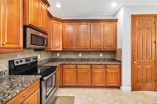 kitchen featuring light tile patterned floors, decorative backsplash, stainless steel appliances, and dark stone counters