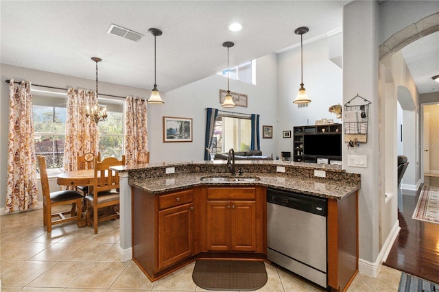 kitchen with stainless steel dishwasher, dark stone counters, sink, and hanging light fixtures