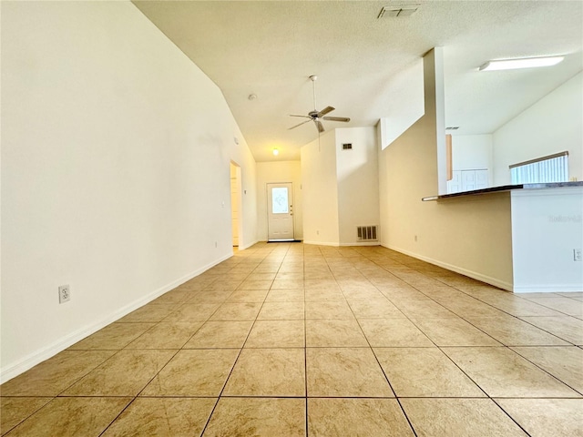 unfurnished room featuring ceiling fan, light tile patterned flooring, a textured ceiling, and vaulted ceiling