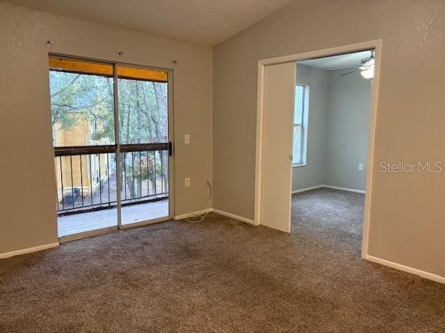 unfurnished room featuring lofted ceiling, plenty of natural light, and dark colored carpet