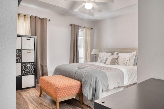 bedroom with hardwood / wood-style flooring, ceiling fan, and a tray ceiling