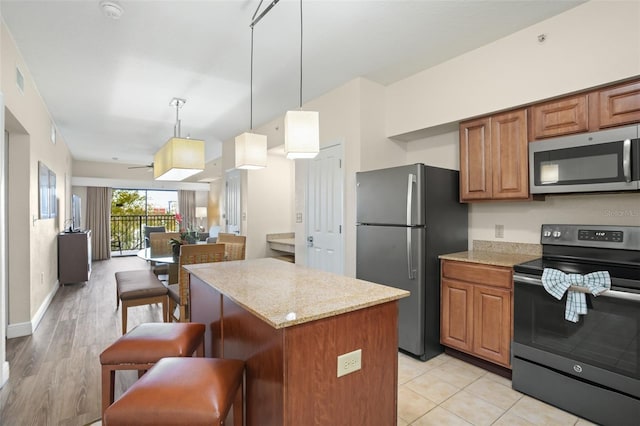 kitchen featuring hanging light fixtures, light stone counters, a center island, a breakfast bar, and stainless steel appliances