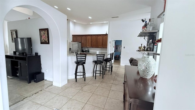 kitchen with a kitchen bar, light tile patterned floors, dark brown cabinetry, and stainless steel fridge