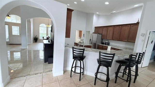 kitchen with a high ceiling, light stone countertops, stainless steel fridge with ice dispenser, kitchen peninsula, and a breakfast bar area