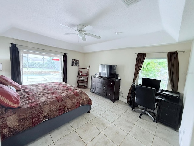 bedroom featuring ceiling fan, multiple windows, and a tray ceiling