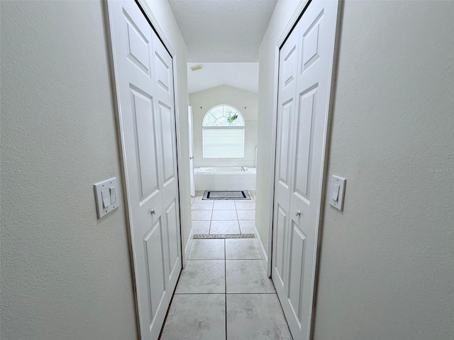 corridor with light tile patterned floors and lofted ceiling