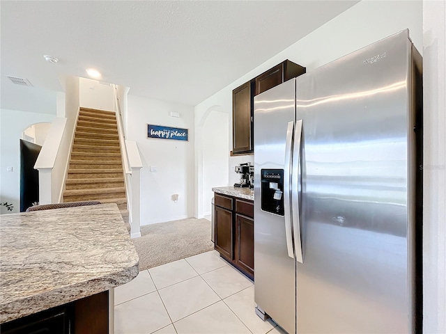 kitchen with stainless steel fridge with ice dispenser, dark brown cabinets, light colored carpet, and light stone countertops