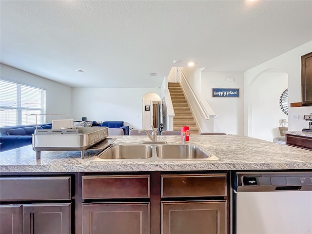 kitchen with sink, dark brown cabinets, stainless steel dishwasher, and a center island with sink