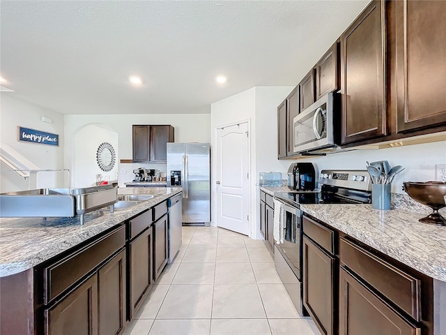 kitchen with dark brown cabinets, a center island with sink, stainless steel appliances, and light tile patterned flooring