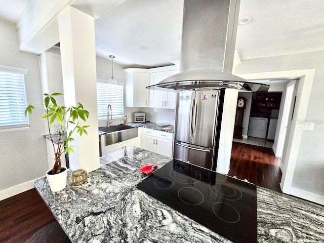 kitchen with island range hood, stainless steel refrigerator, black stovetop, washer / clothes dryer, and white cabinets