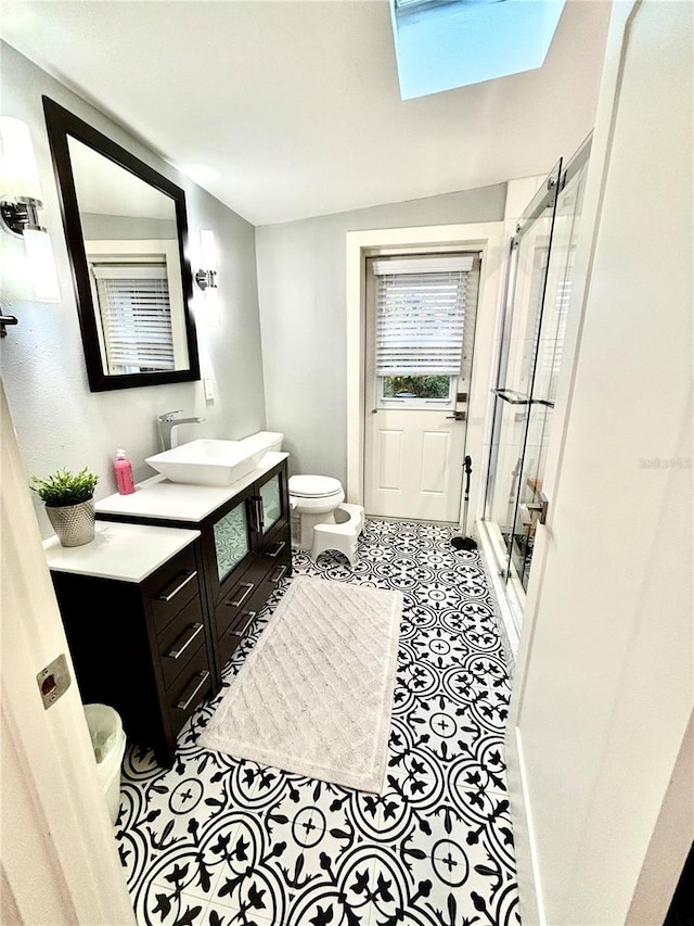 bathroom with a skylight, vanity, a shower with shower door, and toilet